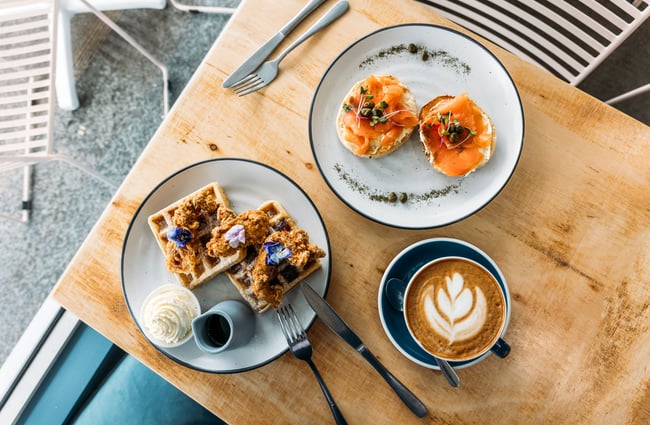 A flatlay of a bagel, waffles and coffee on a table.