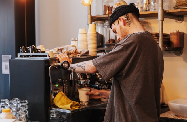 Barista on a coffee machine behind the counter.