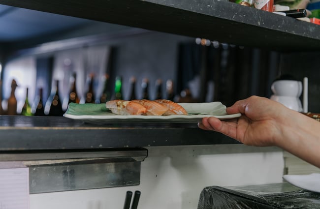 A worker grabbing a plate of prepared salmon sushi.