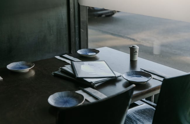 A black table, set up with plates and cutlery next to a big window.
