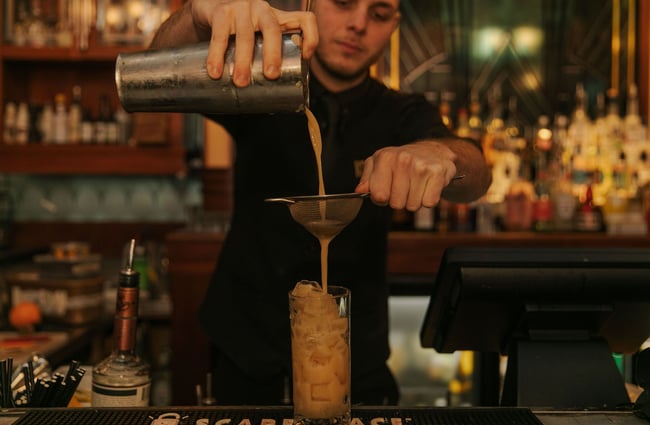 Bartender pouring cocktail into glass filled with ice on bartop