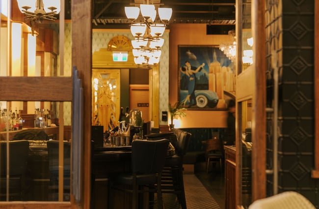 Looking through door of art deco bar with New York artwork on wall and gold doorframe feature blurred in the background