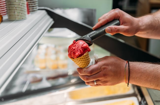 A hand scooping a gelato into a cone.