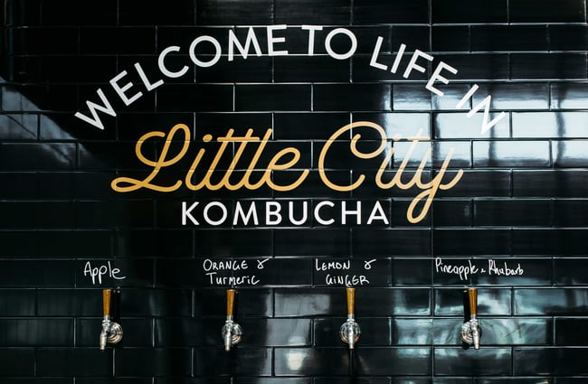 A black tiled wall with six flavours of kombucha on tap.