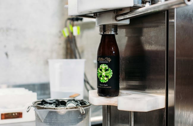 A machine filling up the bottles with a Little City Kombucha label.