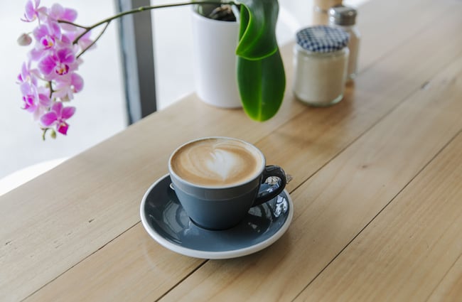 A flat white in a grey cup and saucer on a wooden table.