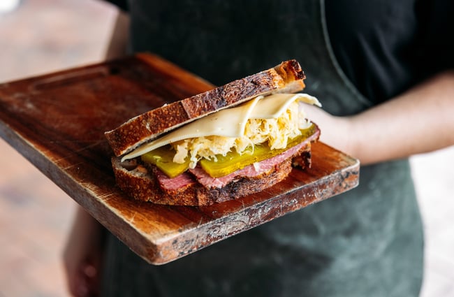 A close up of a cheese, pickle and pastrami sandwich.