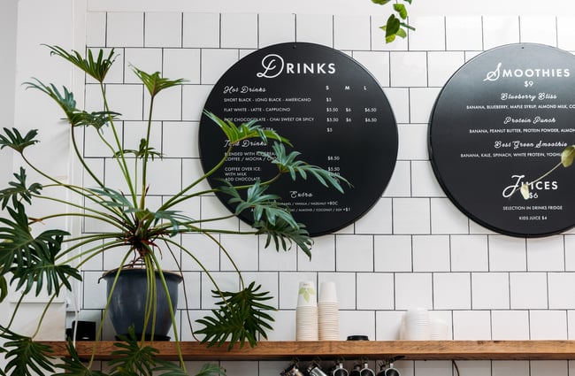 A black drinks menu on a whte tiled wall.