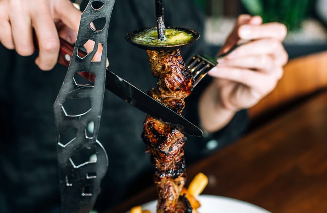 Close up of  someone cutting their meat on a skewer.