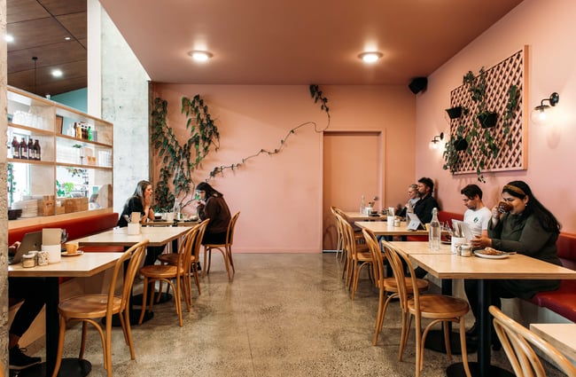 Customers sitting at tables inside a peach coloured cafe.