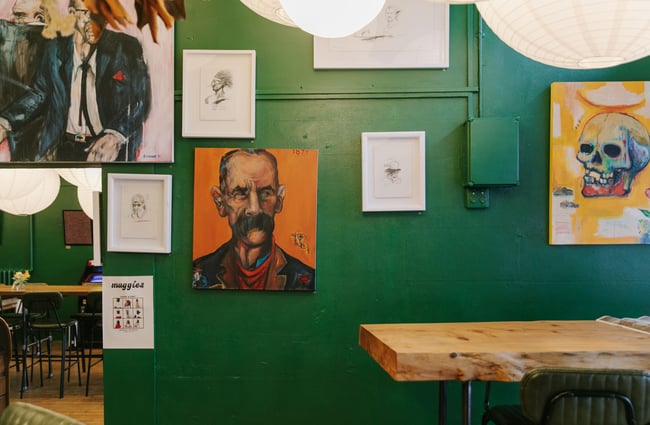 Framed works of art on display on dark green walls inside Maggies cafe Dunedin.