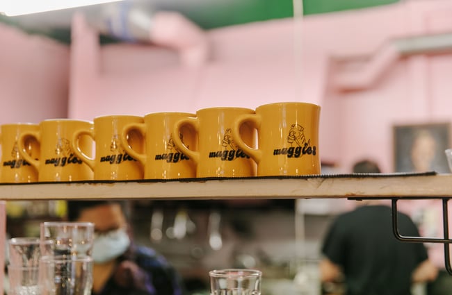 A close up of yellow mugs on a shelf that all say 'Maggies'.