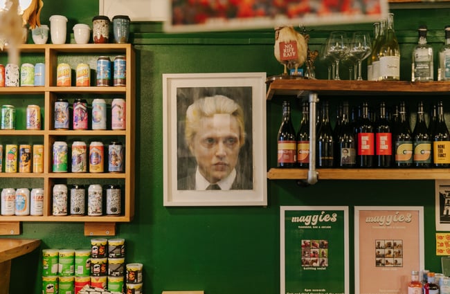 A framed portrait of Christopher Walken on a wall alongside bottles and cans of beer.