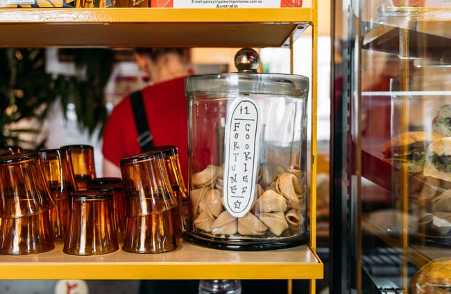 A jar of 1 dollar fortune cookies on cafe shelf next to glasses
