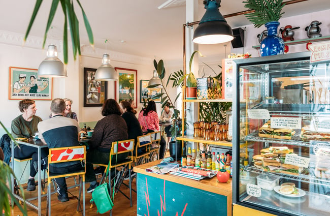 Groups of diners sitting at table together inside a colourful cafe filled with plants