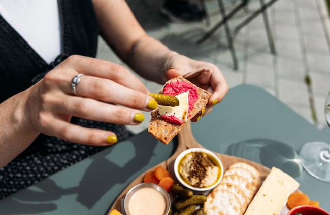 A pickle being placed on to a cracker with pink hummus.
