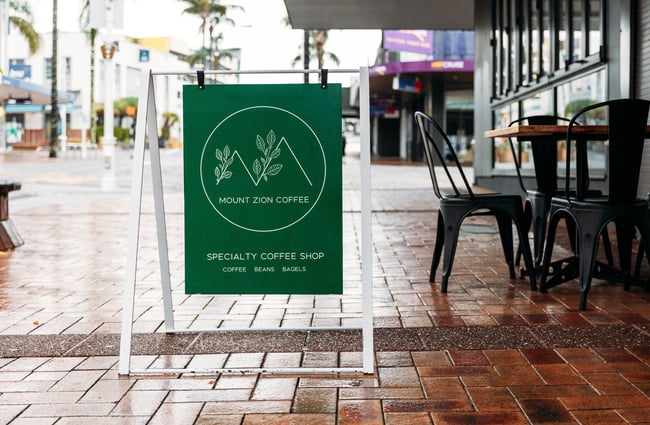 A green 'Mount Zion Coffee' sign on a footpath.