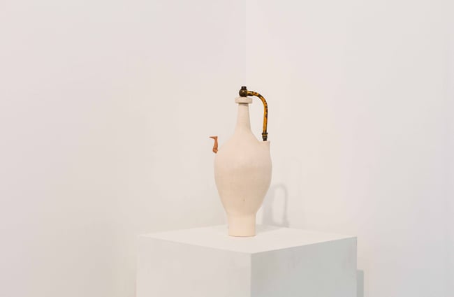 A white vase on display on a white plinth.