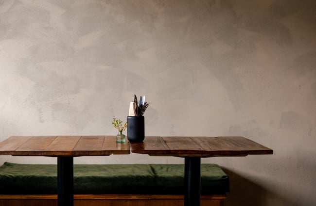 Wooden tables next to a green squab on a bench seat.