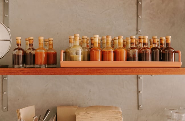 A wooden shelf filled with glass bottles of Mexican sauces.