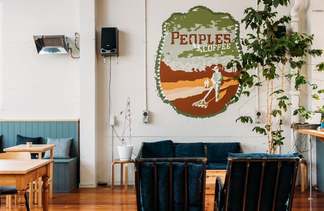 A large 'Peoples Coffee' sign on a wall behind a couch in a cafe.