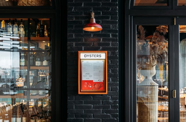 A close up of a sign that says 'Oysters' on a black wall.