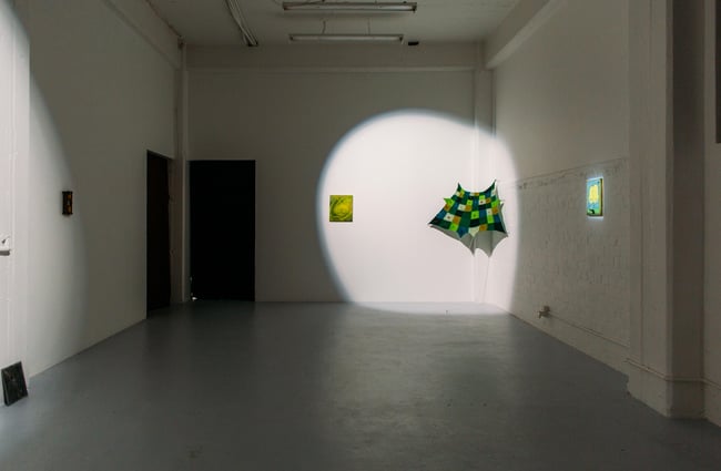 Two green works on display in a corner with a bright spot light shining on both works.