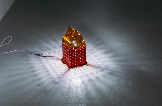 A close up of a sculpture of a house on the floor with a bright light shining from the inside.