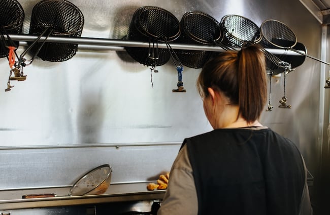 A female staff member stands in front of the deep fryers.