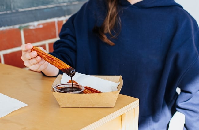 A female holds up a churro that is dripping with chocolate sauce.