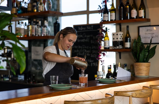 A woman pouring a cocktail at a bar.