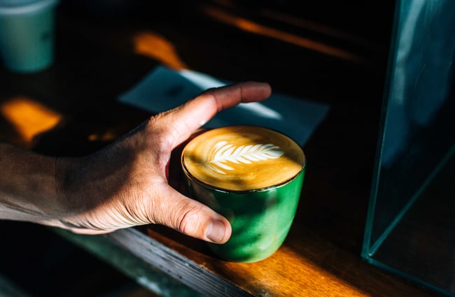 Hand holding a flat white in a green ceramic cup from Proof and Stock, New Plymouth.