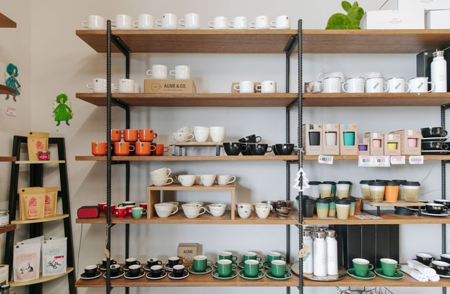 A wooden shelf with black structure displaying cups for sale.