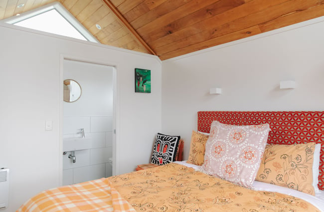 Inside a small eco-friendly wood slatted celling hut with an orange bedding.