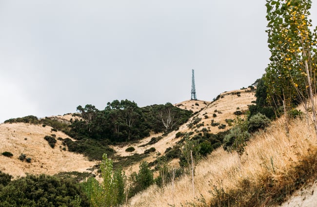 View of dry brown hills and trees with an aerial tower on top.