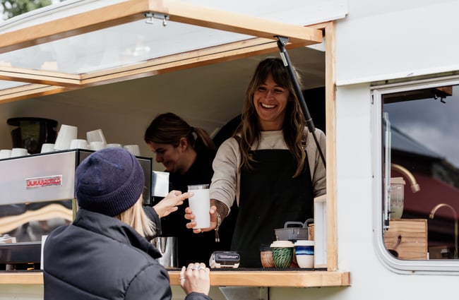 A customer being served a takeaway coffee from a caravan.