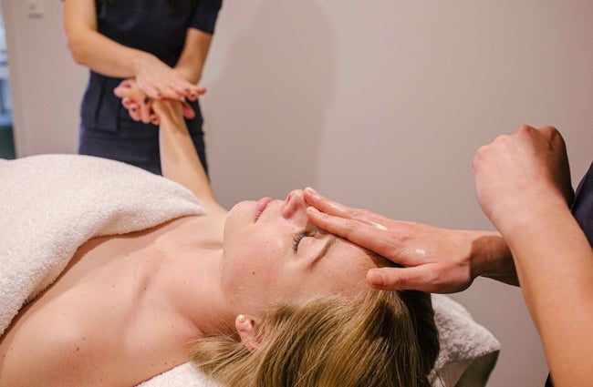 Woman receiving a hand and face massage from two therapists.