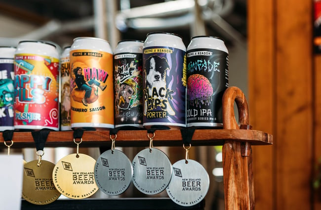 Close up of vibrant illustrations on the labels of Rhyme and Reason's beer cans, with 2023 New Zealand Beer Awards gold and silver medals hanging below respective brews.