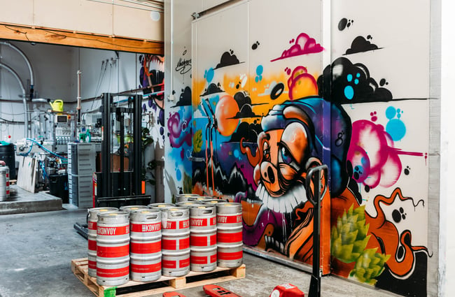 Kegs of beer sitting on a pallet beside a wall with a big graffiti artwork inside Rhyme and Reason, Wānaka.
