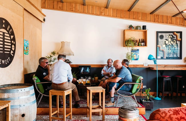 A group of older men sit and chat around a table of half-drunk pints inside Rhyme and Reason, Wānaka.