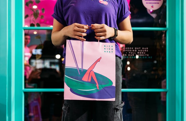 A staff member holding a paper bag with pink legs on it.