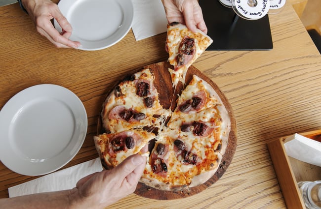 Hands grabbing for a cheese and ham pizza.
