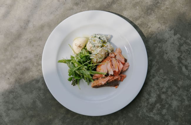 A white plate with potato salad, salmon and a green salad on the side.