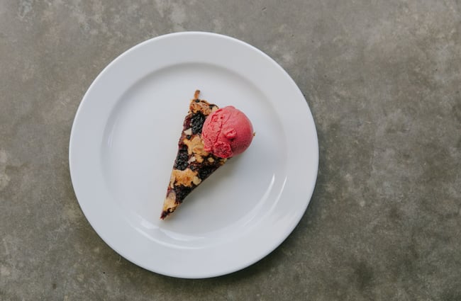 A slice of a berry pie with a scoop of berry ice cream on the top.