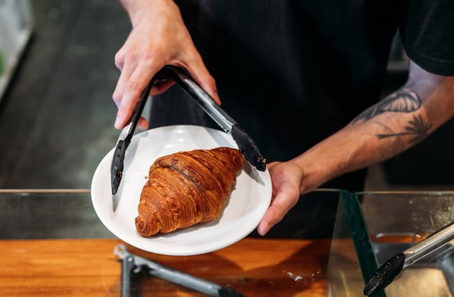 Someone holding tongs next to a croissant on a plate