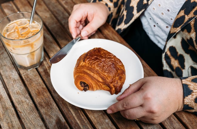 Pain au chocolat on a plate next to an iced coffee with a stainless steel straw