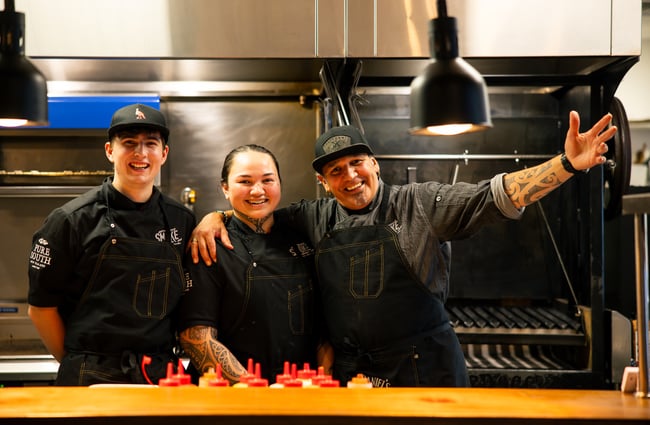 Three chefs posing to camera in a kitchen.