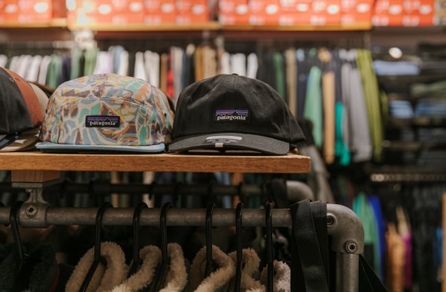 Patagonia caps sitting on a wooden shelf above clothing racks at Stencil.