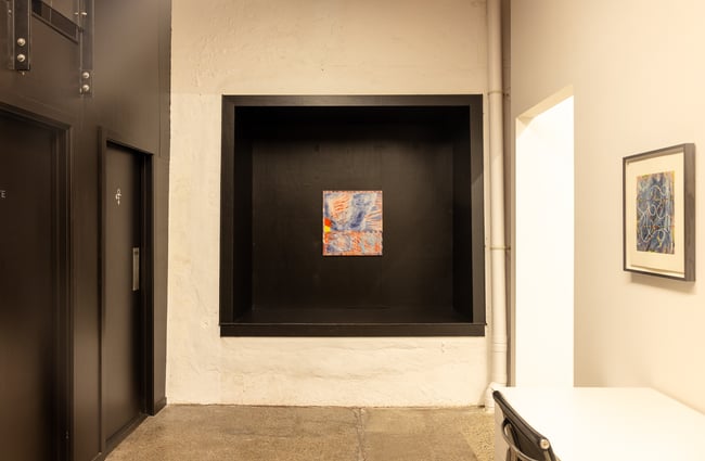 A corner of a gallery with a work of art displayed on a black wall.