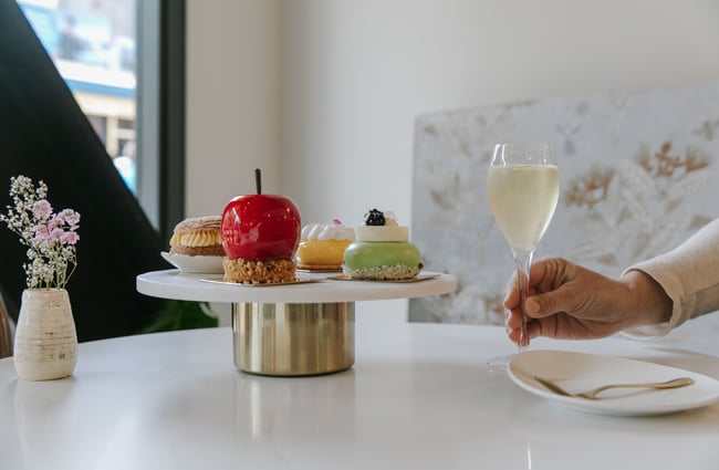 A hand holding a glass of champagne next to sweet cakes on a white table.